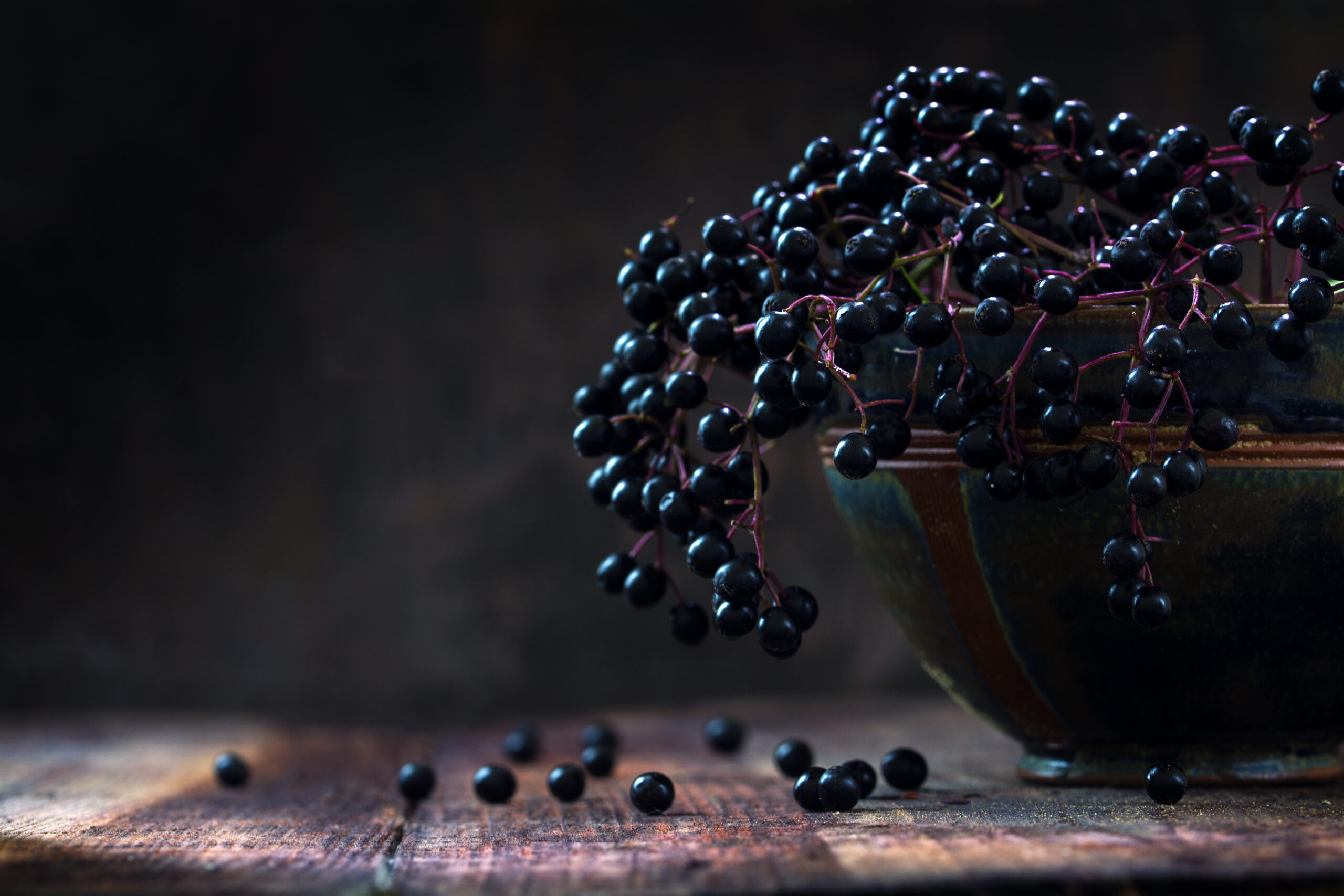 Black elderberries bunch (Sambucus nigra) in an old clay bowl and some berries on a rustic wooden table
