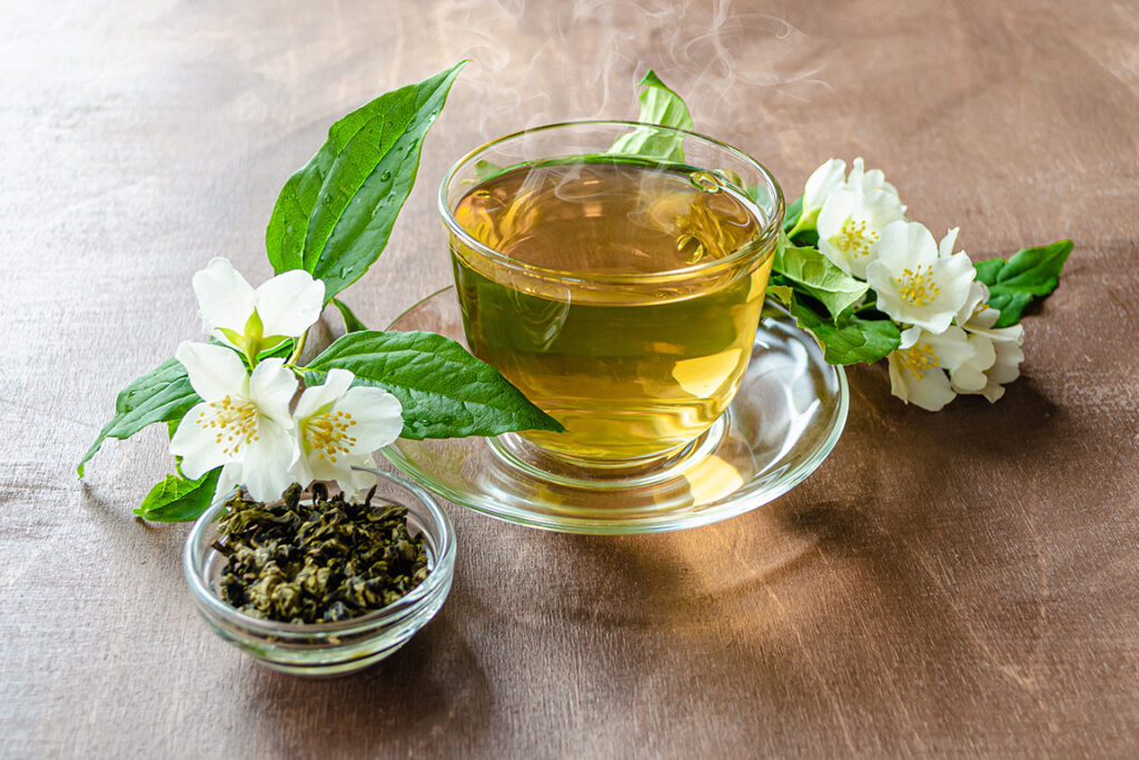 Cup of jasmine tea with loose tea leaves and white jasmine blossoms